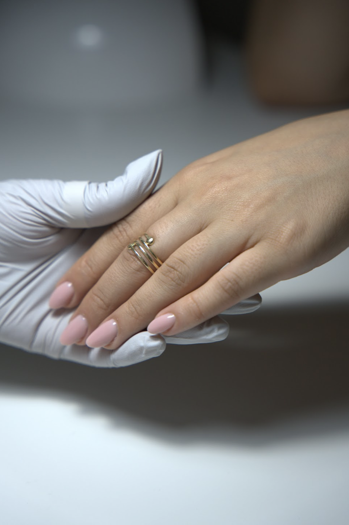 A fresh, glossy nude-pink manicure with a gold ring