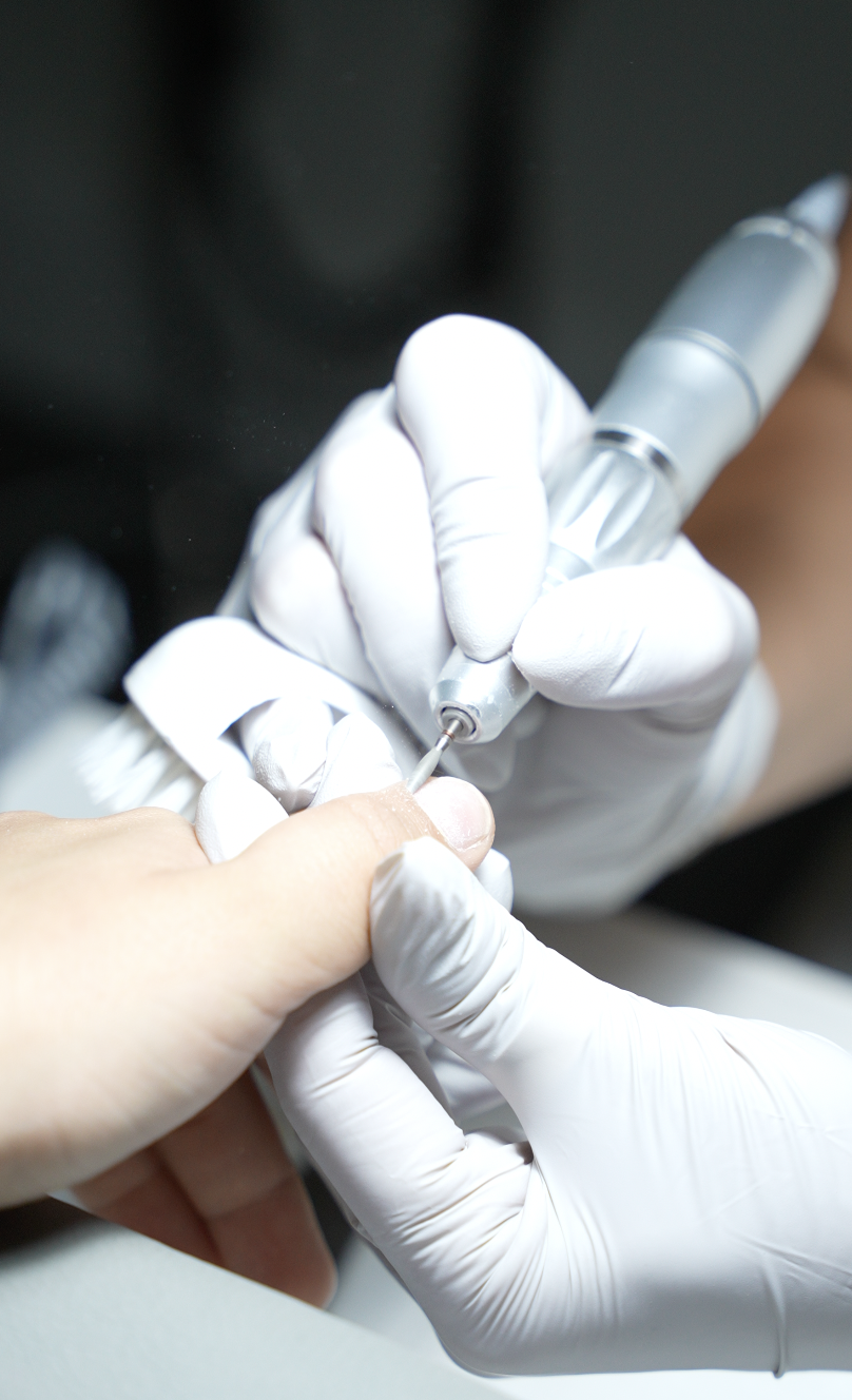 A close-up of a nail technician prepping a nail with an e-file